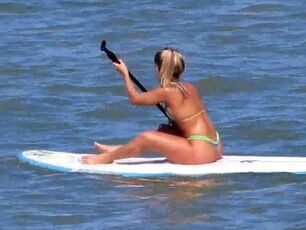 Captivating caboose in g-string swimsuit on surfboard.